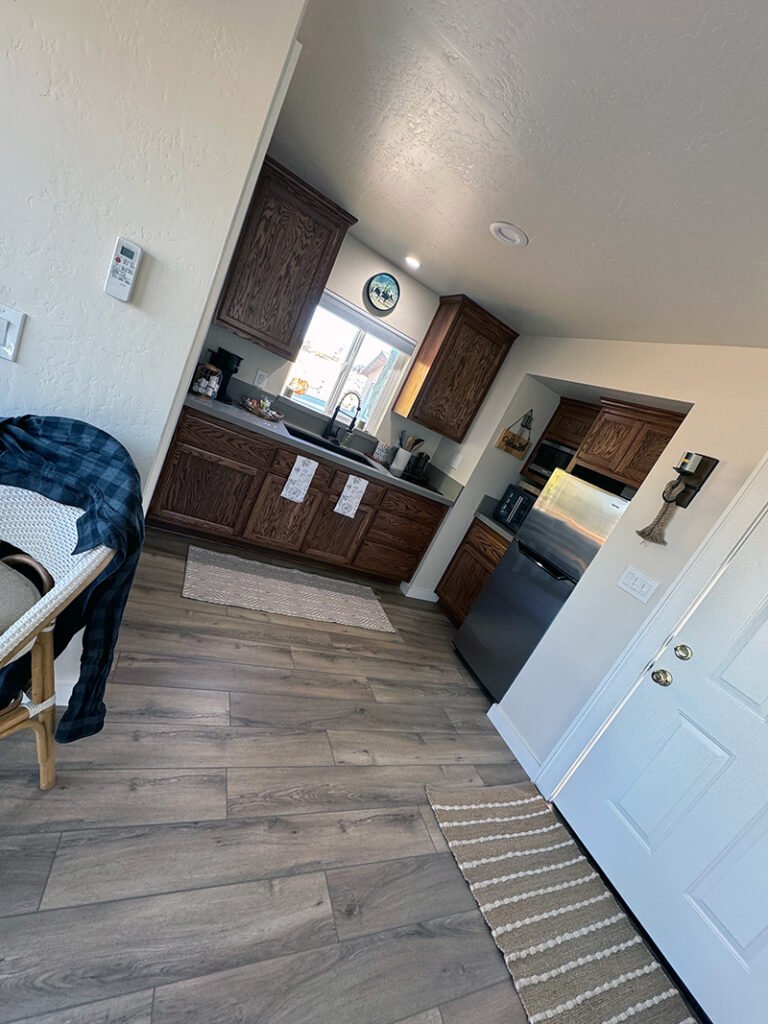 - Warm Kitchen Interior A kitchen with dark wood cabinets, stainless steel appliances, and a window above the sink. White towels hang from cabinet handles, and a coffee maker sits on the counter. A chair with a plaid shirt is visible near the entrance.